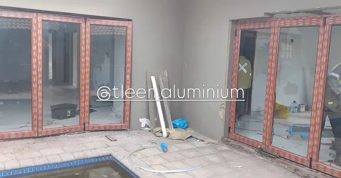 Wood-look aluminium folding doors beside a swimming pool, protective film still on