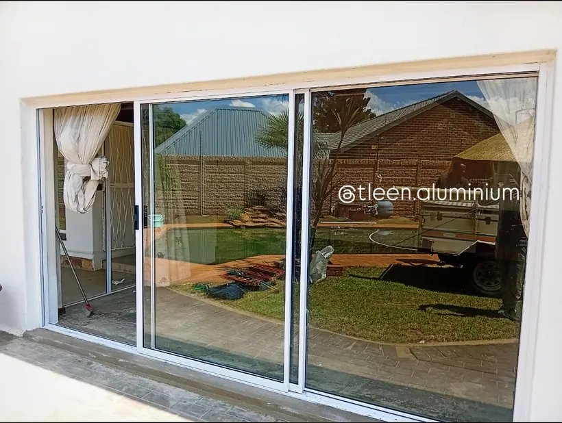 Wide-span white aluminium sliding door opening onto a covered carport