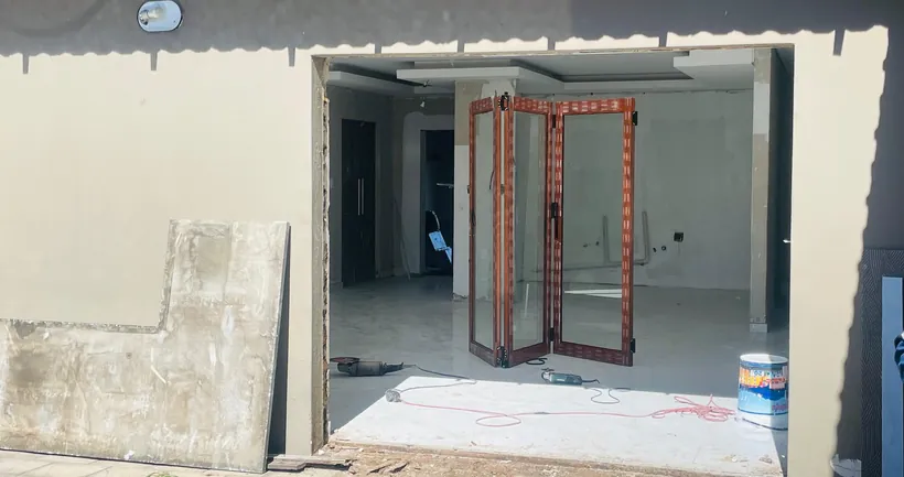 Wide opening cut through a wall with wood-look aluminium folding doors set into it, protective film on the frames and angle grinders still lying on the floor
