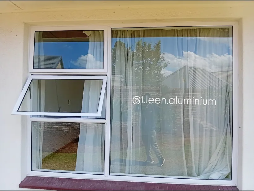 White aluminium top-hung window in a bedroom with curtains