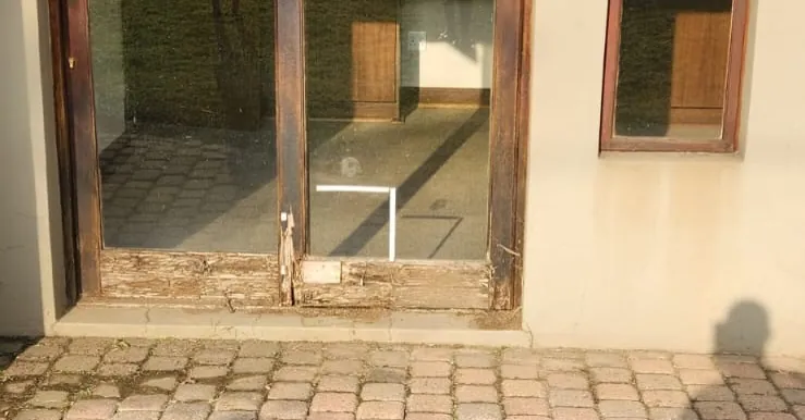 Rotten timber door frame at the base, rotted through above a paved threshold